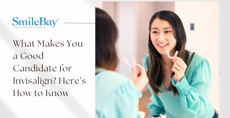 Woman smiling in the mirror while holding an Invisalign clear aligner, symbolizing suitability for treatment.